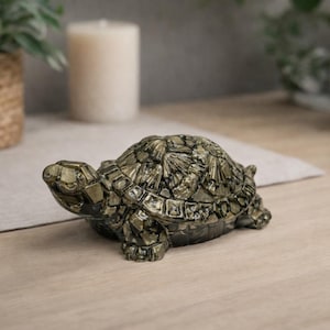 Puede incluir: Figura decorativa de tortuga con caparazón tipo mosaico en tonos dorados y verdes. La tortuga es una escultura detallada, perfecta para la decoración del hogar. La figura está colocada sobre una superficie clara.
