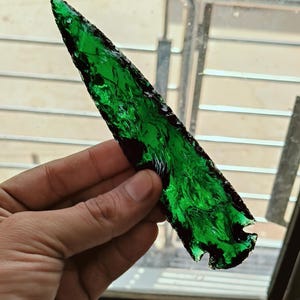 May include: A green obsidian arrowhead with a dark green and black marbled pattern.