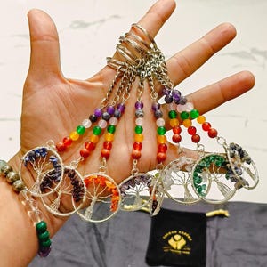 Puede incluir: Un juego de siete llaveros de árbol de la vida de chakra. Cada llavero presenta un diseño de árbol de la vida de alambre plateado con un círculo de piedras semipreciosas que representan los siete chakras. Los llaveros están unidos a llaveros plateados.