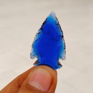 Puede incluir: Una punta de flecha azul hecha de vidrio. La punta de flecha es puntiaguda y tiene un borde afilado.