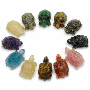 May include: A collection of eleven carved gemstone turtles in various colors, including yellow, green, brown, blue, purple, and pink. Each turtle has detailed shell patterns and is arranged in a circular pattern against a white background.