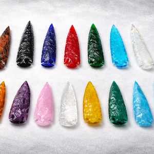 Puede incluir: Una colección de quince puntas de flecha de vidrio de colores. Las puntas de flecha son de varios colores, incluyendo naranja, negro, azul, rojo, verde y blanco. Cada punta de flecha mide unos 7.6 cm de largo.