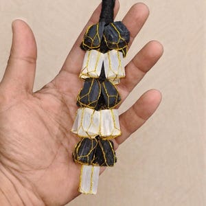 May include: A black and white decorative hanging ornament. The ornament is made of black stones and white, translucent material, all held together with gold wire. The top has a loop for hanging.