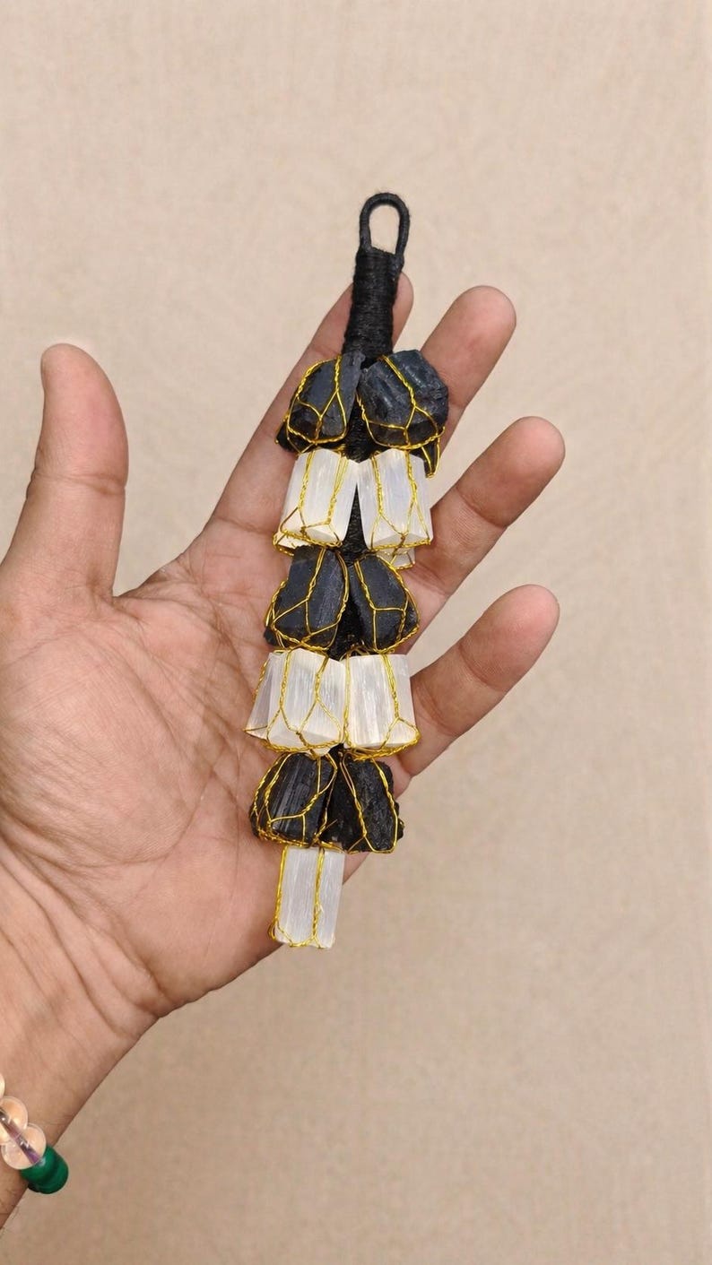 May include: A black and white decorative hanging ornament. The ornament is made of black stones and white, translucent material, all held together with gold wire. The top has a loop for hanging.