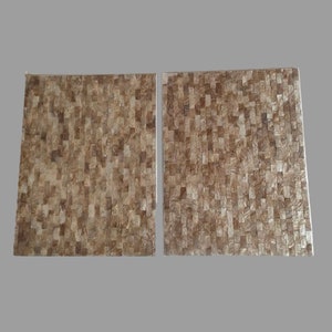 Può includere: Due tovagliette quadrate in mosaico marrone e oro. Le tovagliette sono realizzate con piccoli pezzi irregolari di materiale iridescente.