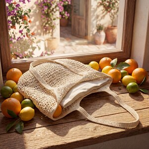 May include: A beige crocheted tote bag with a white lining sits on a wooden surface, surrounded by oranges, lemons, and limes. The bag has two handles and is open, revealing the interior. The scene is illuminated by natural light, suggesting a sunny day.