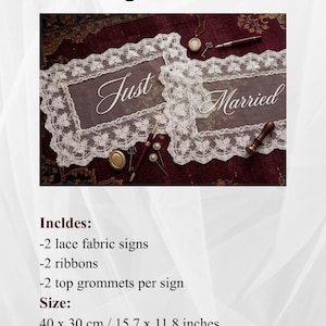 Op de afbeelding: Twee witte kanten stoffen borden met de woorden "Just Married" in sierlijk schrift. Elk bord is 40 x 30 cm groot en bevat linten en grommets. Ze worden gepresenteerd op een bordeauxrode ondergrond.