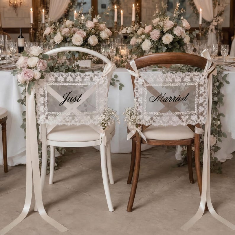 Op de afbeelding: Twee stoelen versierd voor een bruiloft. E&eacute;n witte stoel heeft een bord met "Just" en de andere bruine stoel heeft een bord met "Married". Beide borden zijn omlijst met kant en linten. Bloemschikkingen en kaarsen staan op de achtergrond.