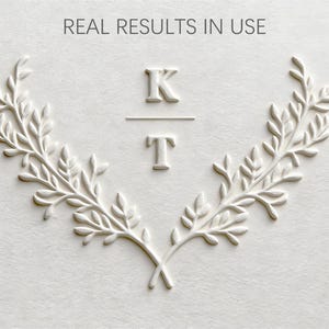 May include: White embossed design with the text "REAL RESULTS IN USE" at the top. The design includes the letters "K" and "T" separated by a horizontal line, surrounded by a symmetrical laurel wreath.