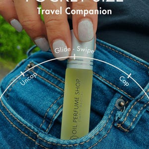 K&ouml;nnte beinhalten: Eine kleine, durchsichtige Glasflasche mit einem silbernen Verschluss und einem gr&uuml;nen Etikett mit der Aufschrift "OIL PERFUME SHOP SIMPLY MAGICAL". Die Flasche befindet sich in einer blauen Jeans-Tasche. Der Text "POCKET SIZE Travel Companion" befindet sich &uuml;ber der Flasche. Die W&ouml;rter "Uncap" und "Cap" befinden sich auf beiden Seiten der Flasche.