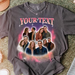 May include: Dark gray t-shirt with the text "YOUR TEXT" in pink and white. The shirt features a graphic of several couples in a circular design. A silver necklace with butterfly accents is visible.