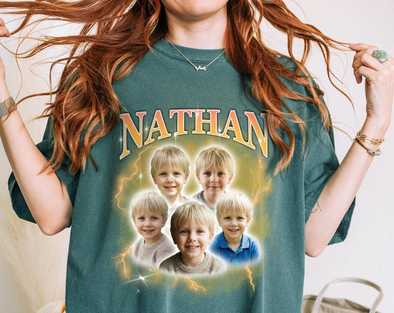 May include: A teal-colored t-shirt with the name "NATHAN" in gold lettering. The shirt features a graphic of five children's portraits surrounded by lightning bolts. The children are wearing various colored shirts.