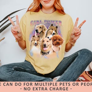 A personalized Comfort Colors 1717 t-shirt in a vintage, faded black or "Pepper" color, featuring a custom digital portrait of a dog on the front, centered on the chest. The dog is a golden retriever with a happy, smiling expression, its fur rendered in warm, natural tones with subtle artistic effects to give it a "bootleg" or retro graphic look. Below the dog's portrait, its name, "Buddy," is written in a distressed, blocky font, consistent with a vintage aesthetic.