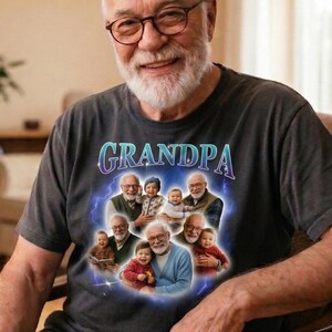 May include: A dark gray t-shirt with the word "GRANDPA" in a blue and purple font. The shirt features a graphic of a grandfather with several children. The man in the image is wearing glasses and smiling.