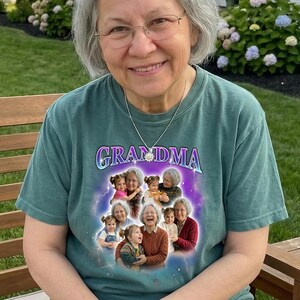 May include: A teal-colored t-shirt with the word "GRANDMA" in a purple and blue font. The shirt features a collage of photos of a woman and children. The woman is wearing glasses and a silver necklace.