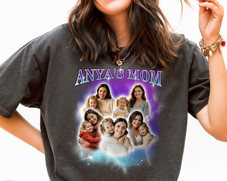 May include: Dark gray t-shirt with the text "ANYA'S MOM" in a blue and purple gradient. The shirt features a graphic of several women and children in a cloud-like design with lightning bolts.