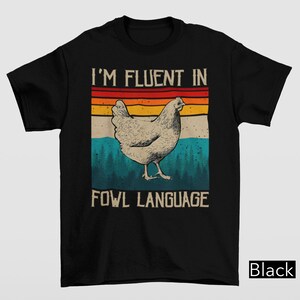 May include: Black t-shirt with a vintage-style graphic of a chicken and the text "I'm fluent in fowl language".