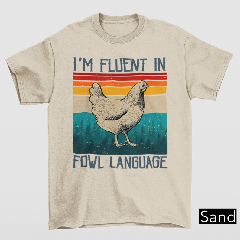 May include: A beige t-shirt with a vintage-style graphic of a chicken and the text "I'm fluent in fowl language".
