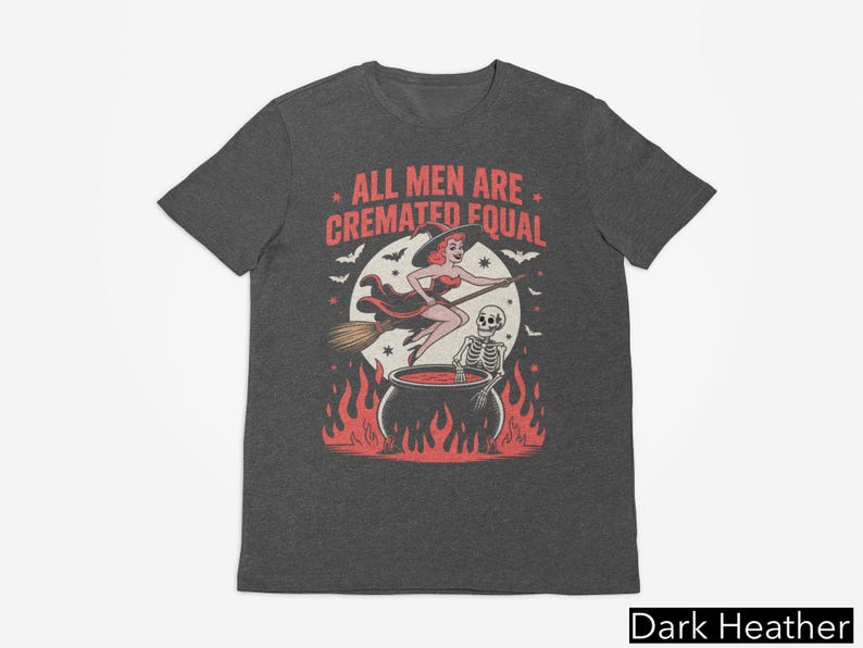 May include: Dark heather gray t-shirt with a Halloween-themed graphic. The design features a witch on a broom, a skeleton, and a cauldron with flames. The text reads "ALL MEN ARE CREMATED EQUAL."