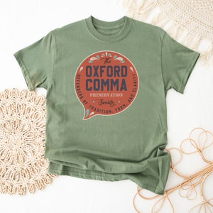 May include: A green t-shirt with a red circle graphic that says "The Oxford Comma Preservation Society. Defenders of Tradition, Form, and Clarity."