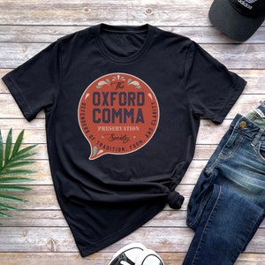 May include: Black t-shirt with a red circle graphic that says "The Oxford Comma" with the text "Defenders of Tradition, Form, and Clarity" around the circle.