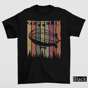 May include: Black t-shirt featuring a retro design with the word "ZEPPELIN" above a black airship illustration. The design includes vertical stripes in various colors, with a forest silhouette at the bottom.