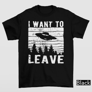 May include: Black t-shirt with a white graphic. The graphic features the text "I WANT TO LEAVE" above a flying saucer and a forest silhouette. The word "Black" is in the bottom right corner.