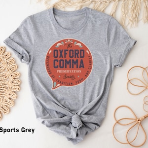 May include: A heather grey t-shirt with a red circle graphic that says "The Oxford Comma Preservation Society. Defenders of Tradition, Form, and Clarity."