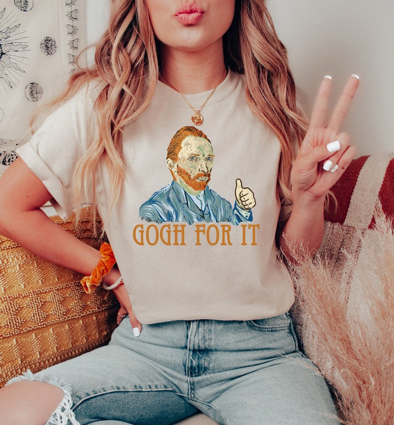 May include: A beige t-shirt with a graphic of Vincent van Gogh giving a thumbs up and the text "GOGH FOR IT".