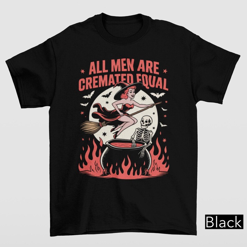 May include: Black t-shirt with a Halloween-themed graphic. The design features a witch on a broom, a skeleton in a cauldron, and the text "ALL MEN ARE CREMATED EQUAL" in pink and white. The image includes bats and flames.