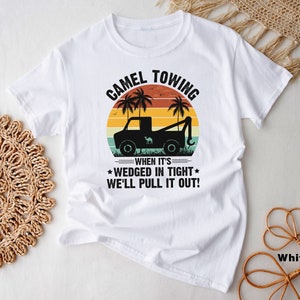 May include: White t-shirt with a vintage-style graphic of a camel towing a car. The graphic includes the text "Camel Towing" and "When it's wedged in tight, we'll pull it out!"