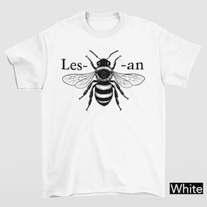 Può includere: T-shirt bianca con un'illustrazione in bianco e nero di un'ape e la scritta "Les- -an". La parola "White" è in un riquadro nero in basso a destra. È un capo d'abbigliamento casual.
