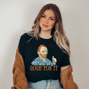 May include: A black t-shirt with a graphic of Vincent van Gogh giving a thumbs up. The text "Gogh for it" is printed below the graphic.
