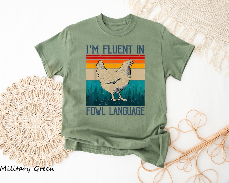 May include: A green t-shirt with a retro-style graphic of a chicken and the text "I'm fluent in fowl language".