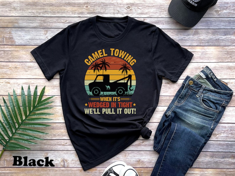 May include: Black t-shirt with a vintage-style graphic of a tow truck pulling a camel. The text reads "Camel Towing When It's Wedged In Tight We'll Pull It Out!"