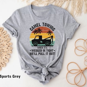 May include: A gray t-shirt with a vintage-style graphic of a tow truck pulling a camel. The text reads "Camel Towing" and "When it's wedged in tight, we'll pull it out!"