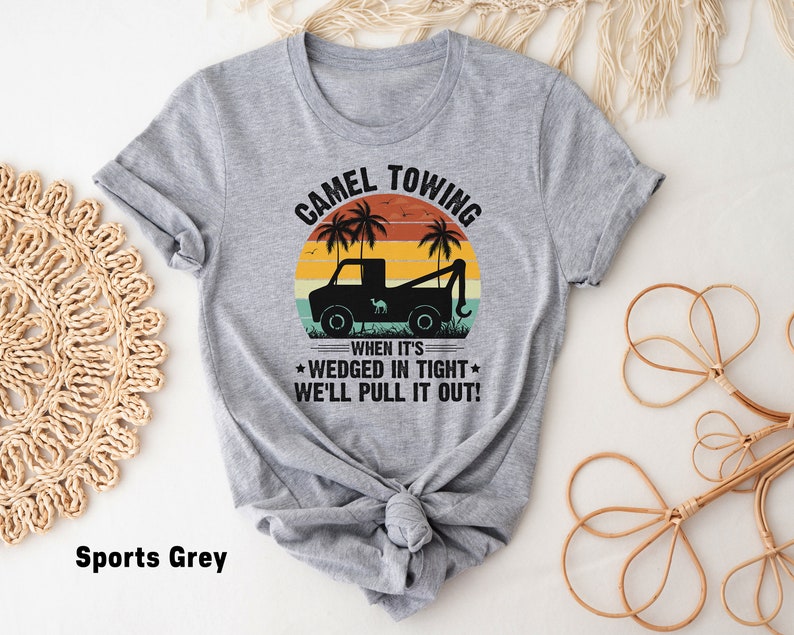 May include: A gray t-shirt with a vintage-style graphic of a tow truck pulling a camel. The text reads "Camel Towing" and "When it's wedged in tight, we'll pull it out!"