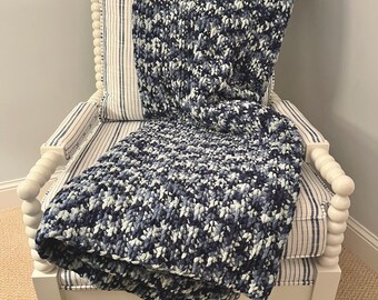 Könnte beinhalten: Ein weißer Sessel mit einem blau-weiß gestreiften Kissen und einer blau-weißen Strickdecke.
