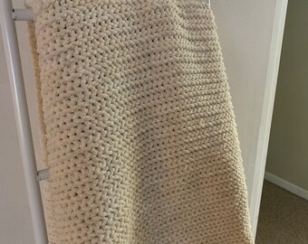 May include: A cream-coloured knitted throw blanket draped over a white ladder.