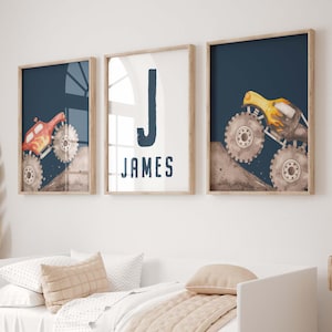 May include: Three framed prints for a child's room. Two prints show monster trucks against a dark blue backdrop. The third print displays the letter "J" and the name "JAMES" in navy blue. The frames are light brown.