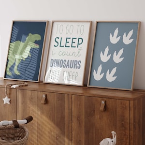 May include: Three framed prints for a nursery or child's room. The print on the left shows a green dinosaur with the text "To go to sleep I count dinosaurs not sheep". The middle print has the text "To go to sleep I count dinosaurs not sheep". The print on the right shows a blue background with white dinosaur footprints.