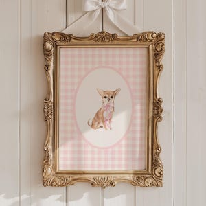May include: A framed print featuring a watercolor illustration of a Chihuahua wearing a pink bow. The print is set against a pink gingham background within an oval frame. The ornate gold frame is suspended by a white ribbon and bow.