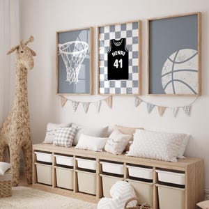 May include: Three framed basketball-themed prints in a child's room. The prints feature a basketball net, a jersey with the name "Henri" and the number 41, and a basketball. The room also has a woven giraffe and a storage bench.