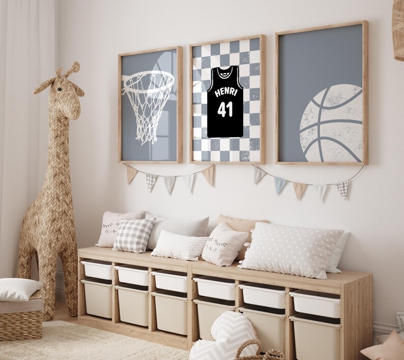 May include: Three framed basketball-themed prints in a child's room. The prints feature a basketball net, a jersey with the name "Henri" and the number 41, and a basketball. The room also has a woven giraffe and a storage bench.
