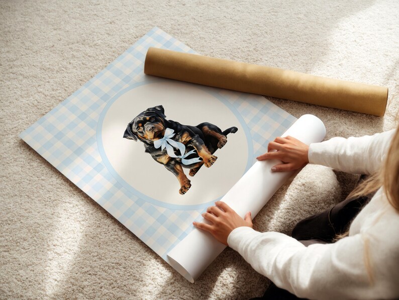May include: A watercolor print of a Rottweiler puppy wearing a blue bow, set against a light blue gingham pattern. The artwork is on a large, rolled-up poster, with a second rolled poster in the background.