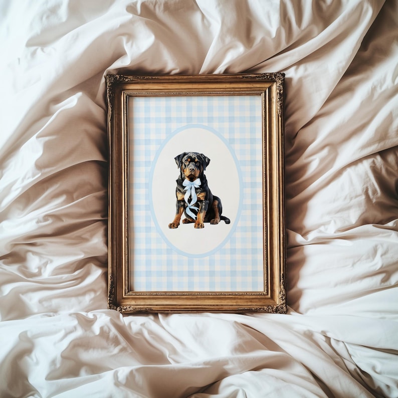 May include: A framed print featuring a Rottweiler dog with a blue bow. The dog is centered in an oval against a light blue and white checkered background. The frame is gold-colored and ornate.