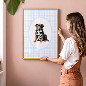 May include: A framed print featuring a Rottweiler dog with a blue bow tie, set against a light blue and white gingham pattern. The dog is centered within an oval frame, adding a touch of elegance to the artwork.