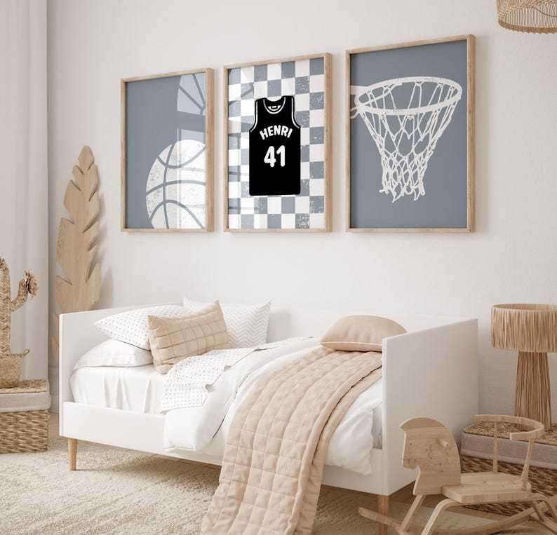 May include: Three framed basketball-themed prints. One shows a basketball, another a jersey with "HENRI 41", and the third a net. The artwork is in neutral tones, with a white bed and decor in the foreground.