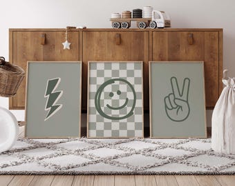 May include: Three framed art prints with a neutral color palette. One features a green lightning bolt, another a green smiley face on a checkered background, and the third a green peace sign hand gesture. The frames are light brown.