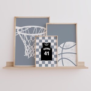 May include: Three framed prints on a wooden shelf. The prints feature a basketball hoop, a basketball jersey with the name "HENRI" and the number "41", and a basketball. The background of the prints is a light grey colour.